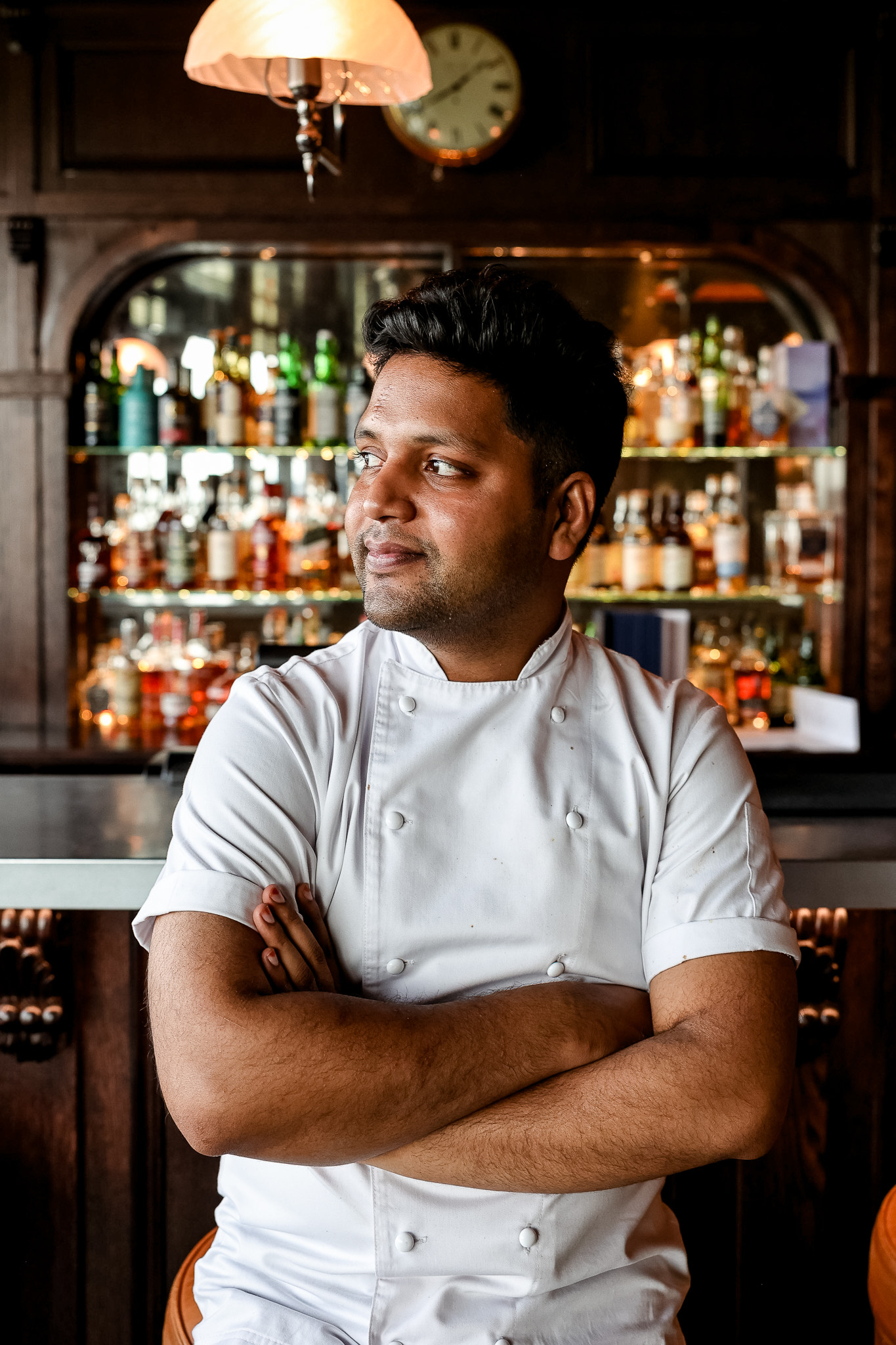Male in a white chef's jacket posed in front of a bar looking out of frame