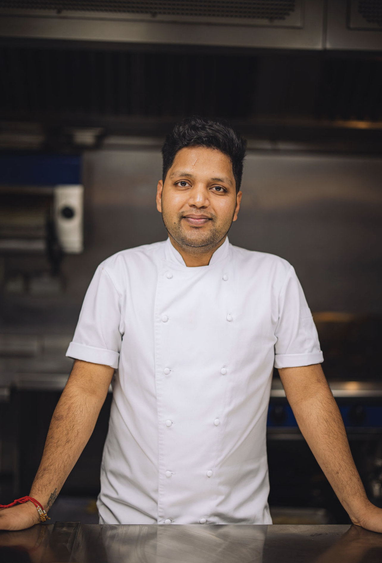 Male chef wearing a white jacket in a kitchen, looking directly to the camera